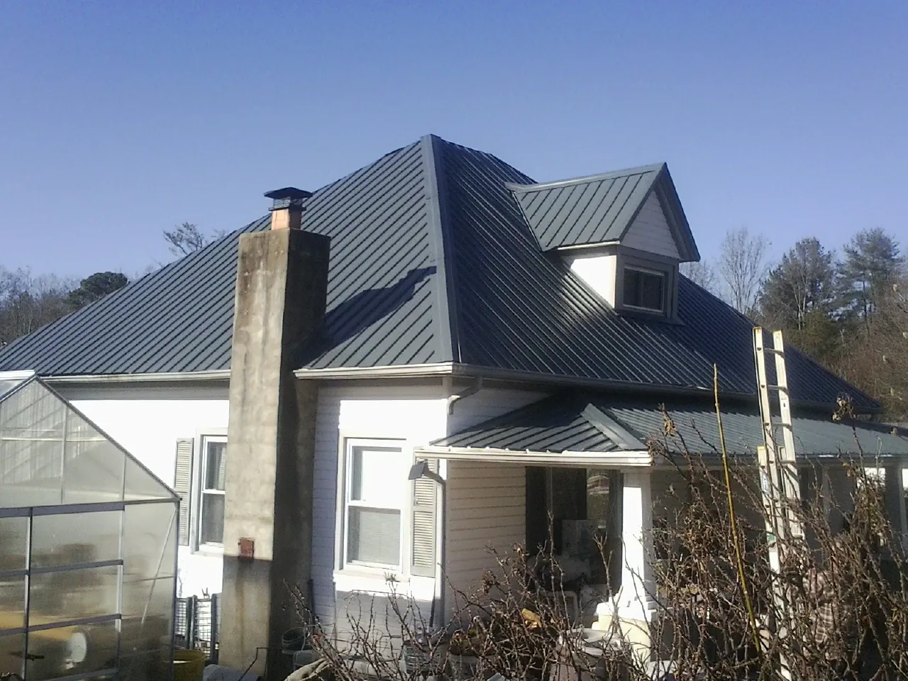 Dark blue standing seam metal roof on a white farmhouse with dormer — Slate & Tile Roof Repair by Roofing Brothers in Cougar