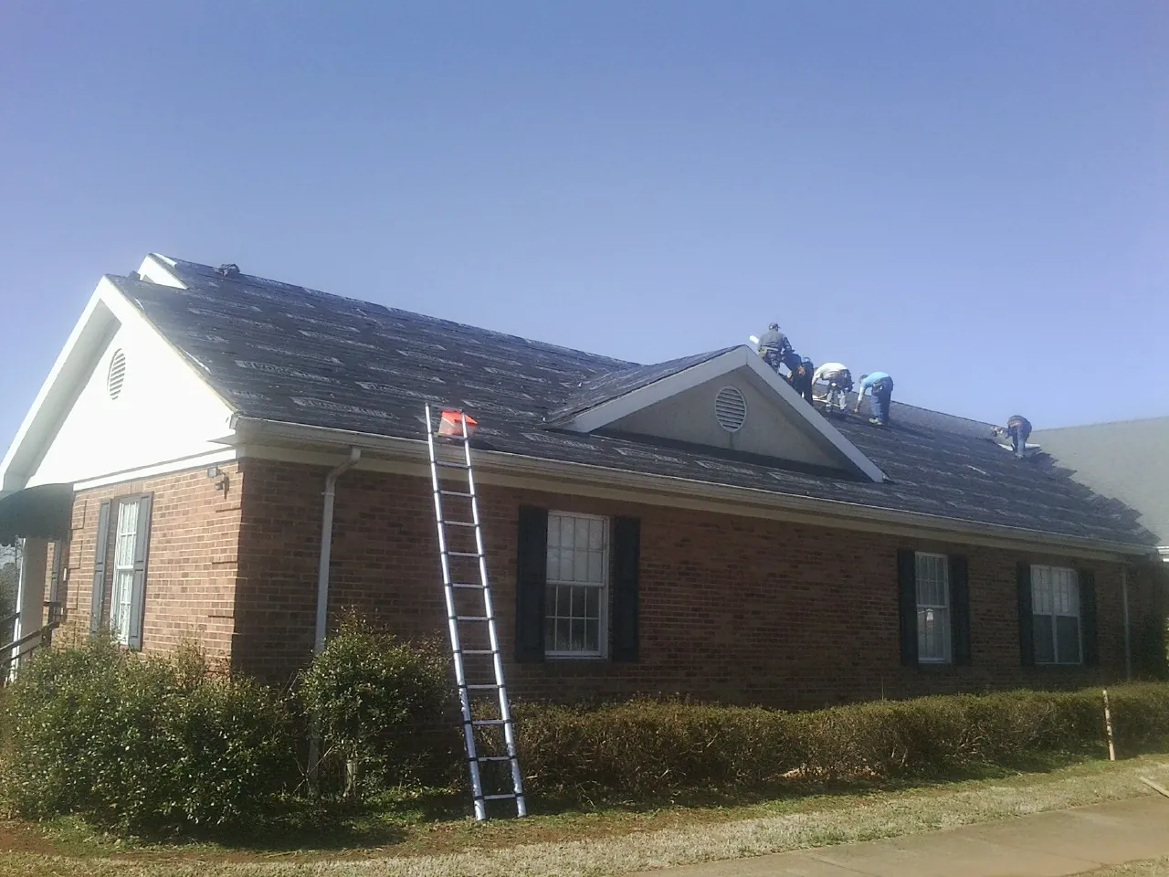 Crew tearing shingles off a brick ranch roof with a ladder set — Metal Roof Repair work by our crew in Cougar