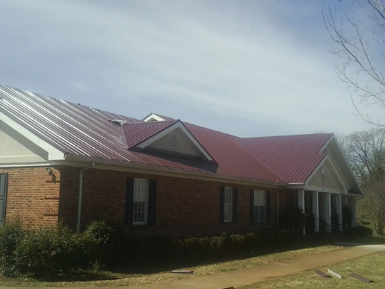 Red metal roof with gabled entries on a long brick building, from a Hail Damage Roof Repair job in Cougar