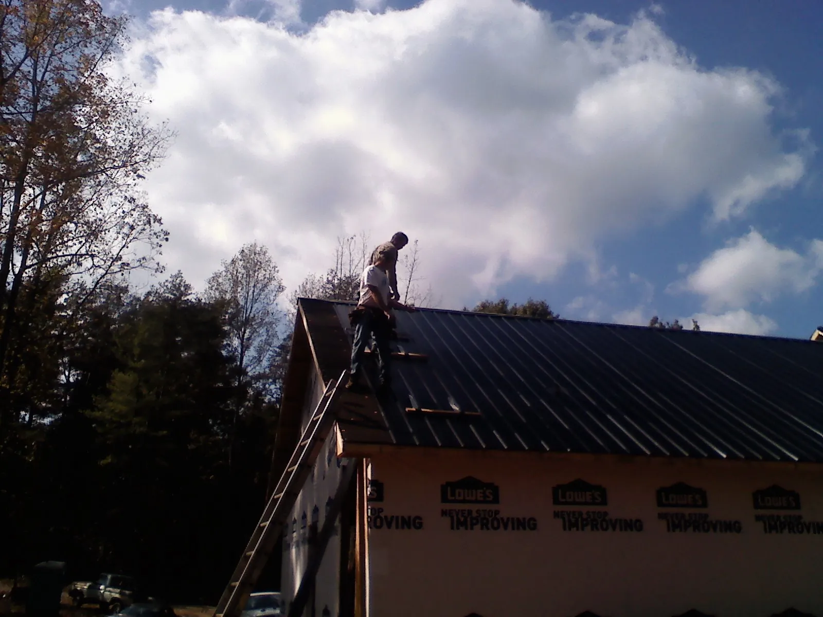 Roofer fastening dark metal panels high against a cloudy sky, from a Roof Inspection job in Cougar