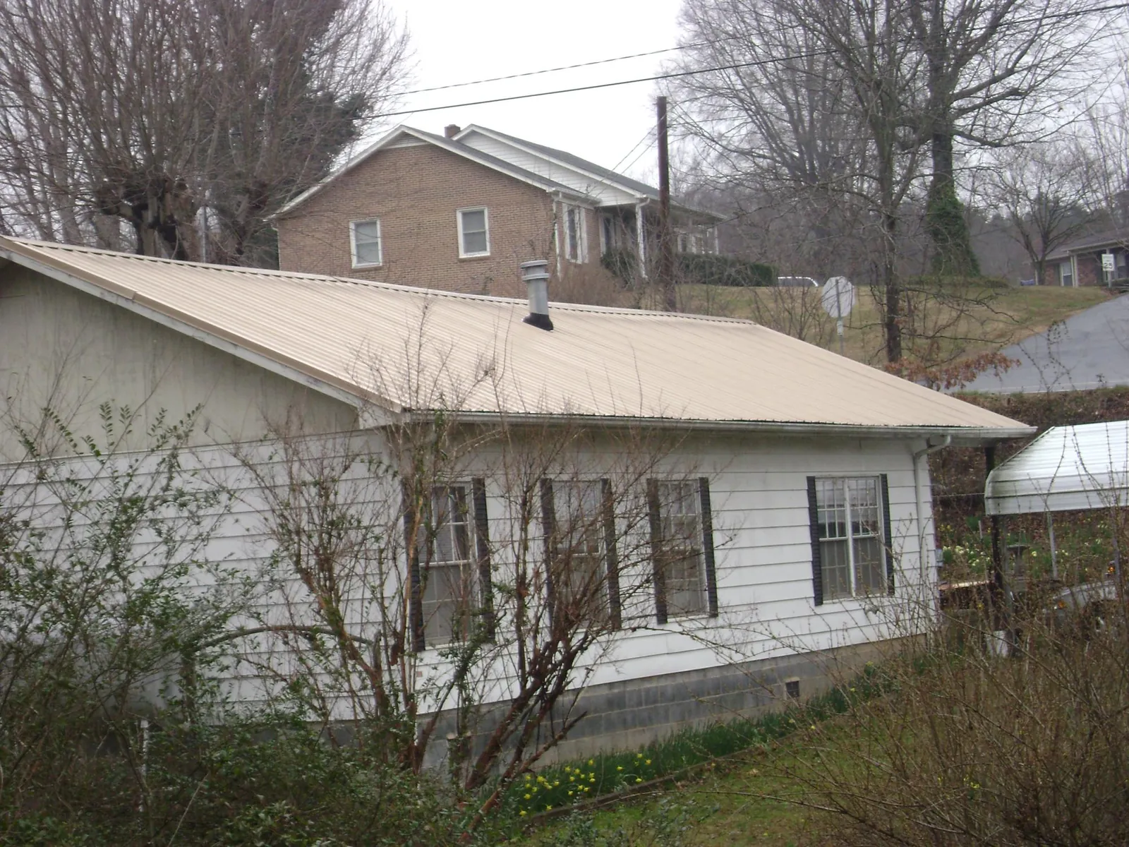 Tan metal roof on a white sided house set into a hillside — Commercial Roofing by Roofing Brothers in Cougar