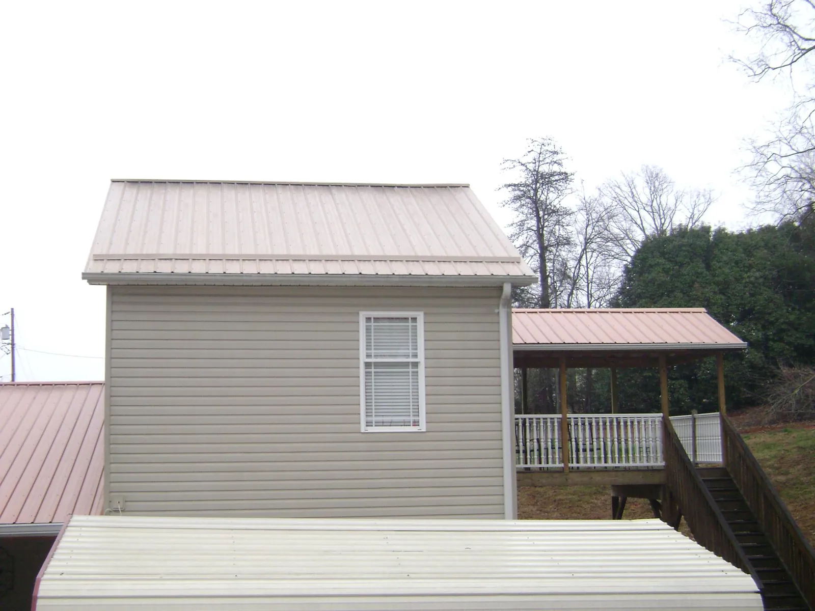 Tan metal roofs on a two story addition and attached porch, from a Roof Replacement job in Cougar